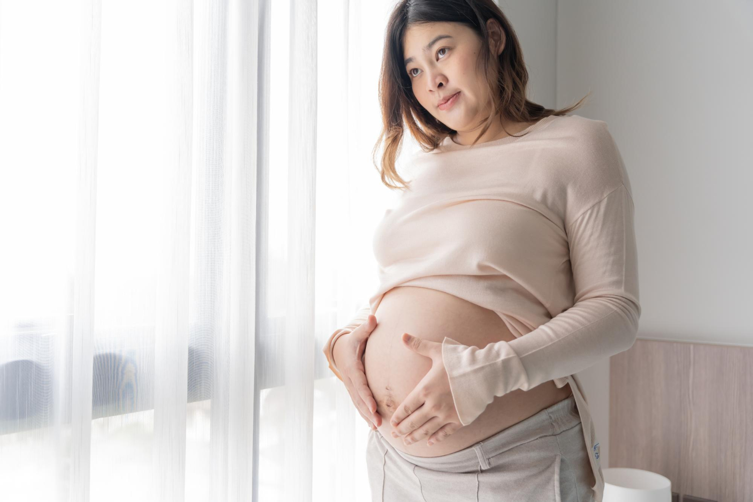 Pregnant asian woman holds hands on belly