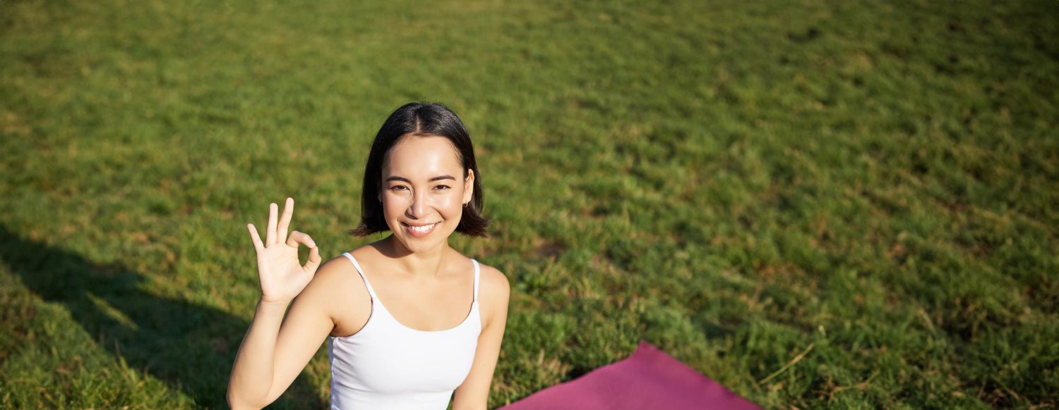 Portrait of asian woman sitting on rubber mat meditating showing okay sign
